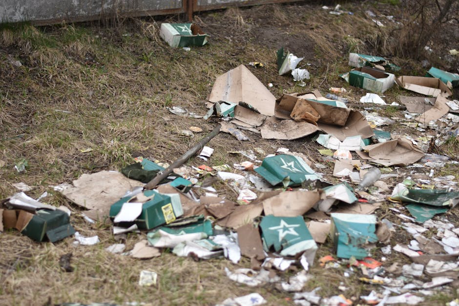 A large pile of black plastic rubbish bags stacked against a tiled wall, with some bags torn open and revealing waste inside. Several discarded plastic bottles and pieces of paper are visible among th